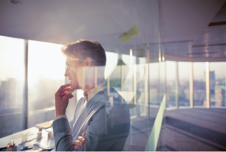 Man standing looking out of office window, contemplating business plans.