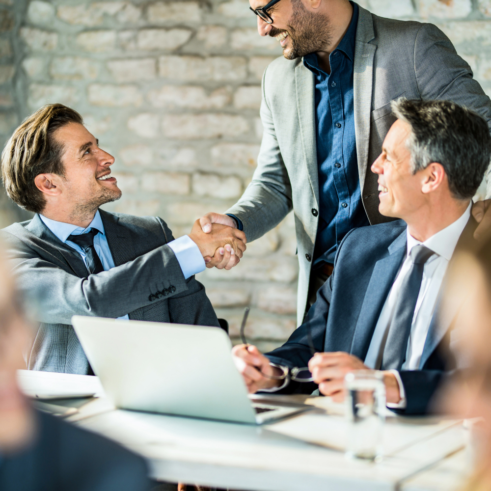2 men shake hands while another man smiles