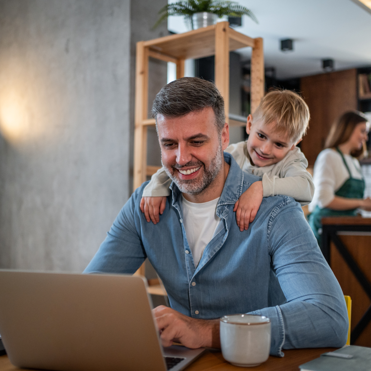 Child looks over dad's shoulder while he works on laptop